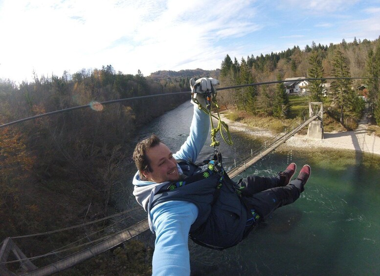 A person bungee jumping with a rope attached to a bridge over a river, surrounded by trees and a clear sky. 3