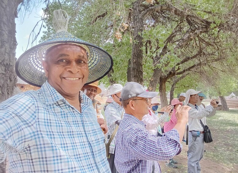 A group of people outdoors, some wearing hats, standing under trees. 4