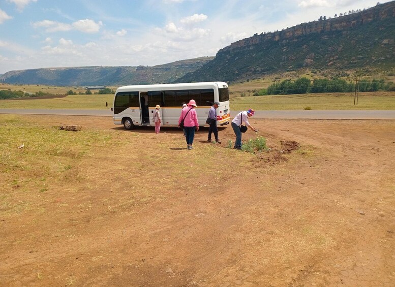 A group of people near a white bus on a dirt road with a mountainous landscape in the background. 5