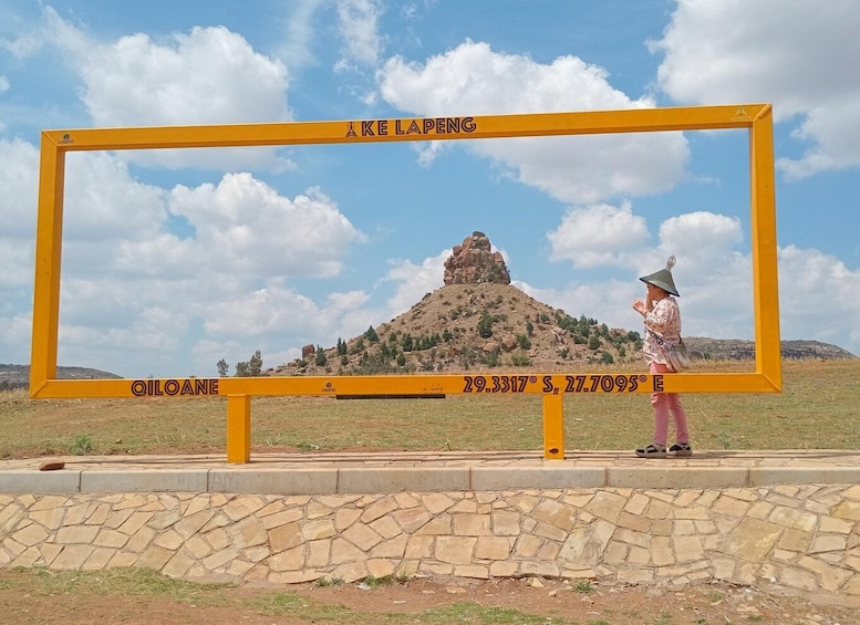 A person standing in front of a yellow sign with coordinates and the name 'KE LAPENG' on a clear day. 2