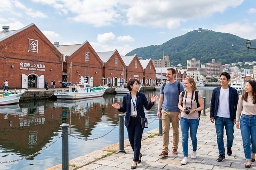 A group of people walking by a waterfront with brick buildings and boats. 1