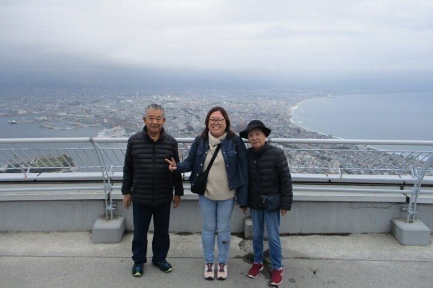 Three people standing on a viewing platform overlooking a coastal cityscape. 4