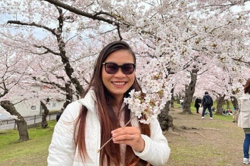 A person holding a branch of cherry blossoms in a park with other people in the background. 4