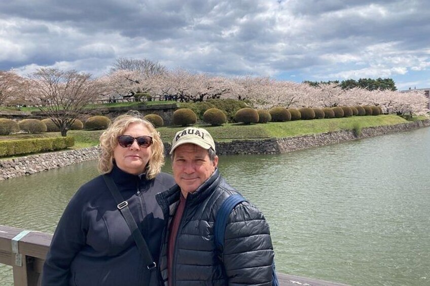 Two people standing by a river with cherry blossoms in the background. 4