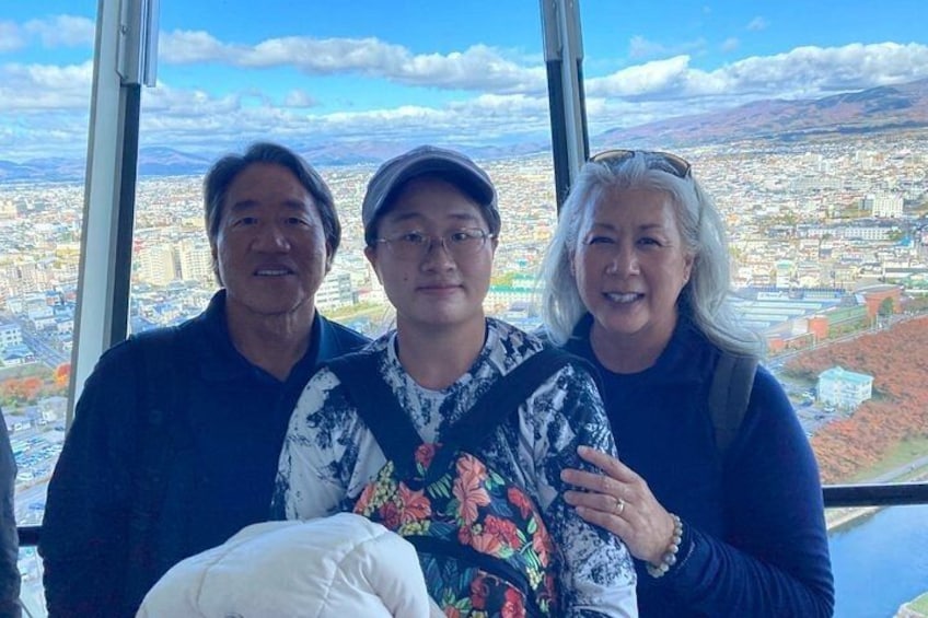 Three people standing in front of a large window with a cityscape view. 5