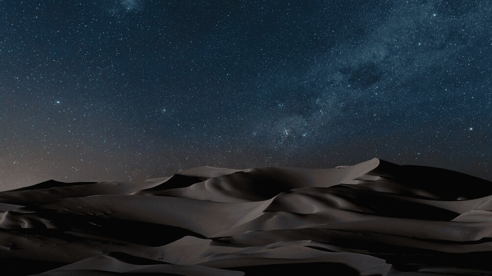 A starry night sky over a desert landscape with sand dunes. 2