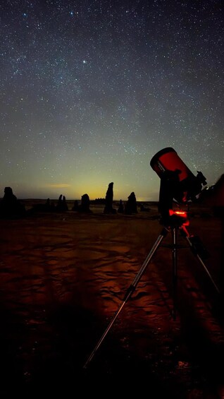 A telescope set up on a tripod in a desert landscape under a starry night sky. 3
