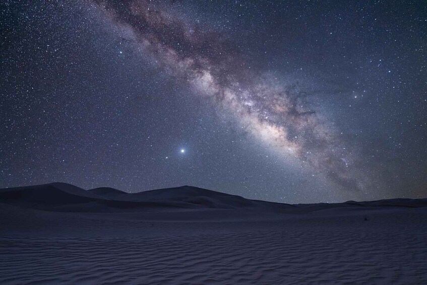 A starry night sky over a desert landscape with sand dunes. 4