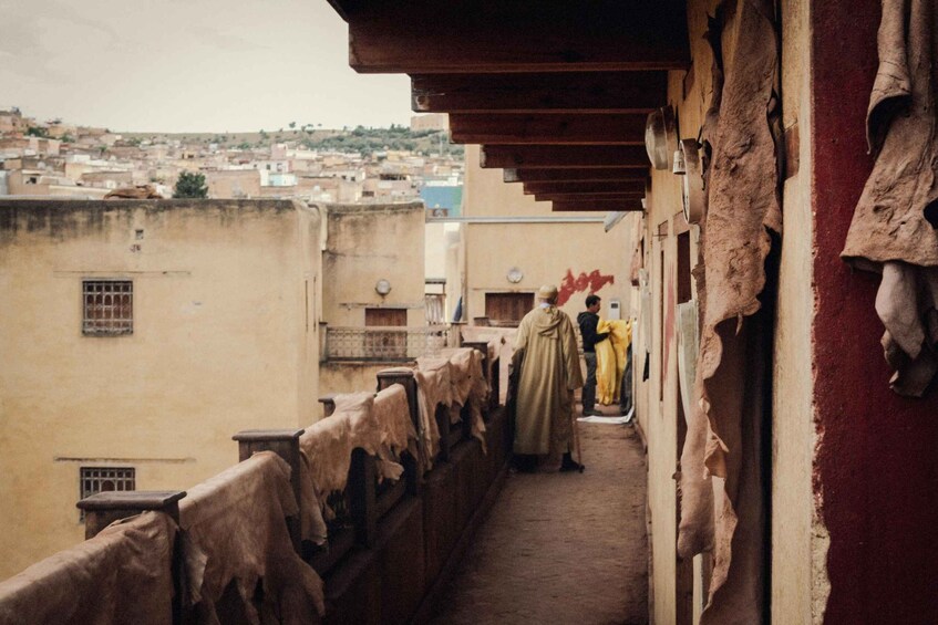 A narrow alleyway with a view of a cityscape, a person in yellow, and a building with a red wall. 3