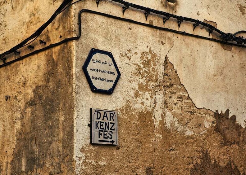 A weathered wall with two signs: one in Arabic and one in German. 5