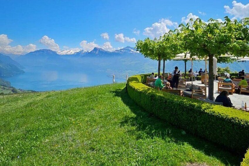 A lakeside café with people dining, surrounded by lush greenery and mountains in the background. 3