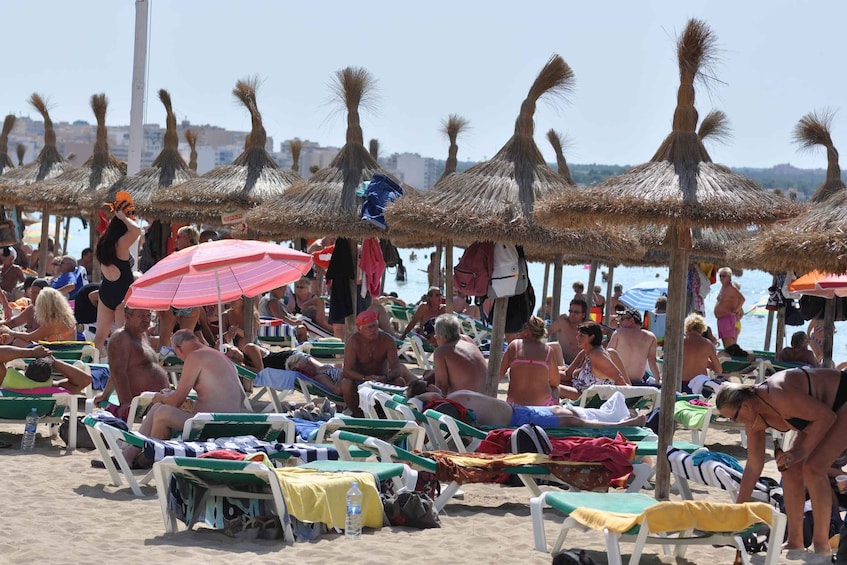 A crowded beach with people sunbathing under thatched umbrellas. 4