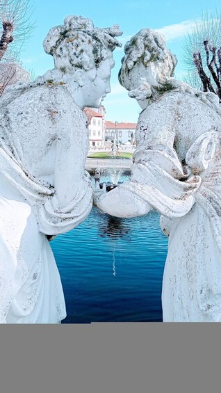 A sculpture of two figures kissing over a body of water with buildings in the background. 4