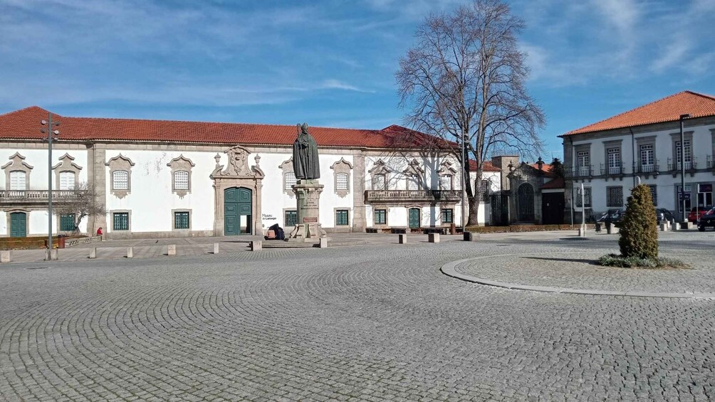 A cobblestone plaza with historic buildings, a statue, and a tree. 5