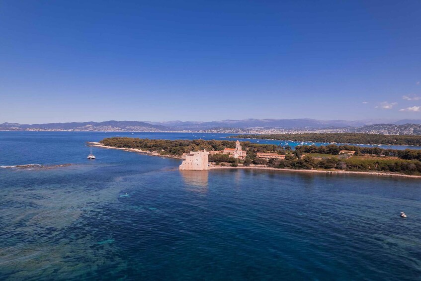 A coastal landscape with a prominent castle, clear blue sea, and distant cityscape. 4