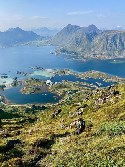 A hiker on a grassy hill overlooking a fjord with mountains in the background. 1