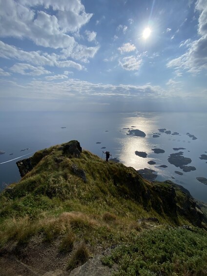 A hiker on a grassy hill overlooking a calm sea with scattered islands under a partly cloudy sky. 5