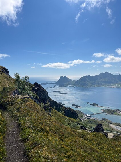 A coastal landscape with a clear sky, a rocky path, and a distant mountain range. 4