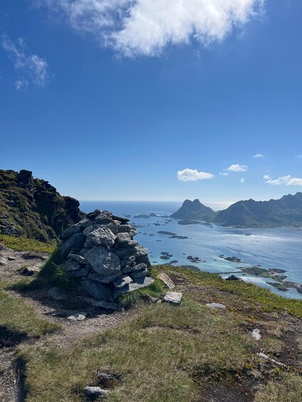 A coastal landscape with a stack of rocks, grassy terrain, and distant mountains under a clear sky. 2
