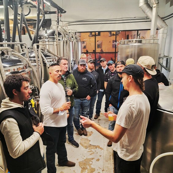 A group of people in a brewery with stainless steel tanks and pipes. 5