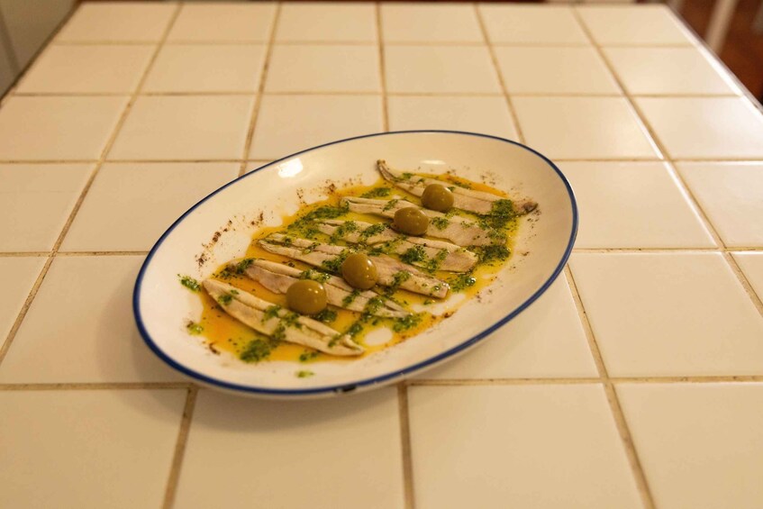 A plate of fish with olives and herbs on a tiled kitchen counter. 1
