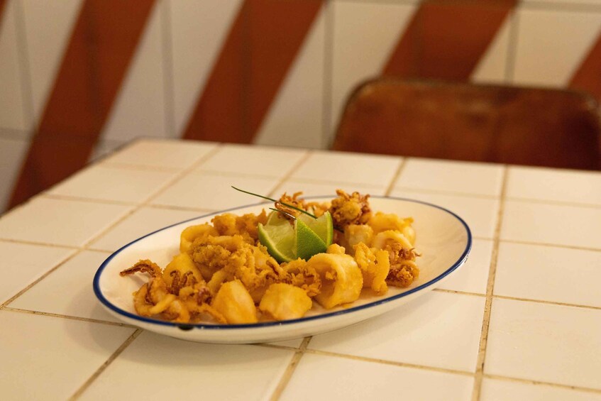 A plate of fried seafood with lime garnish on a tiled table. 3