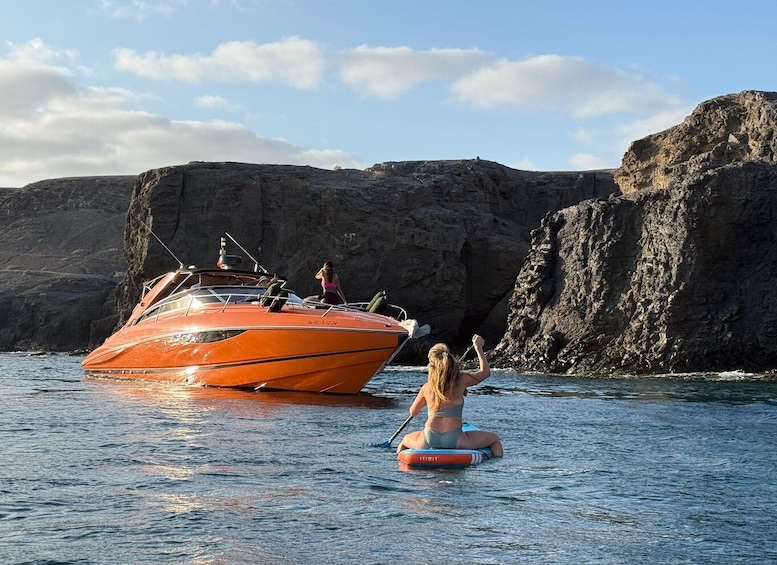 A woman paddleboarding near a rocky coastline with a boat in the background. 2