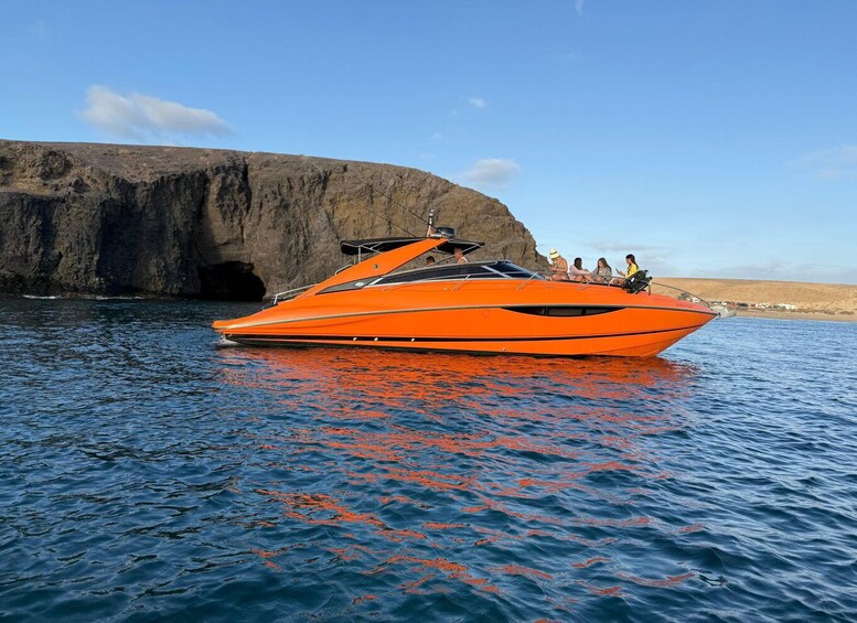 A bright orange speedboat with passengers on a calm sea, near a rocky coastline. 3