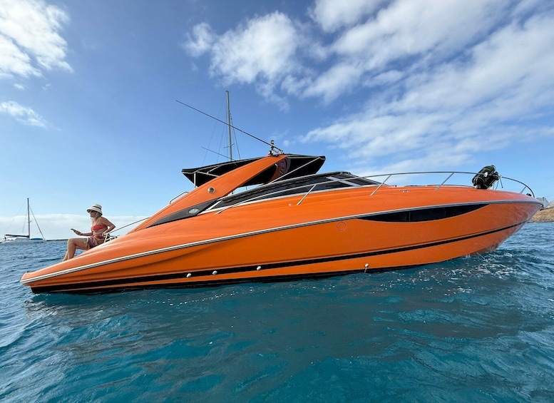 A bright orange speedboat on calm waters with a clear sky and distant sailboats. 5