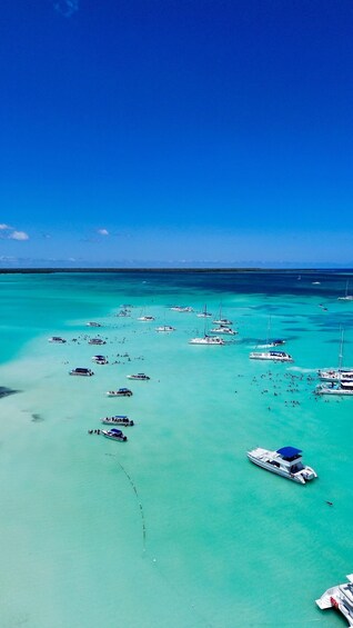 A turquoise sea with numerous boats anchored, clear skies, and distant land. 4