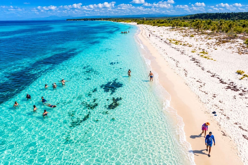 A beach with clear turquoise water, people swimming and walking along the shore. 2