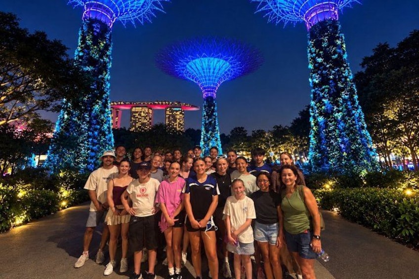 A group of people posing in front of illuminated structures with a large building in the background. 1