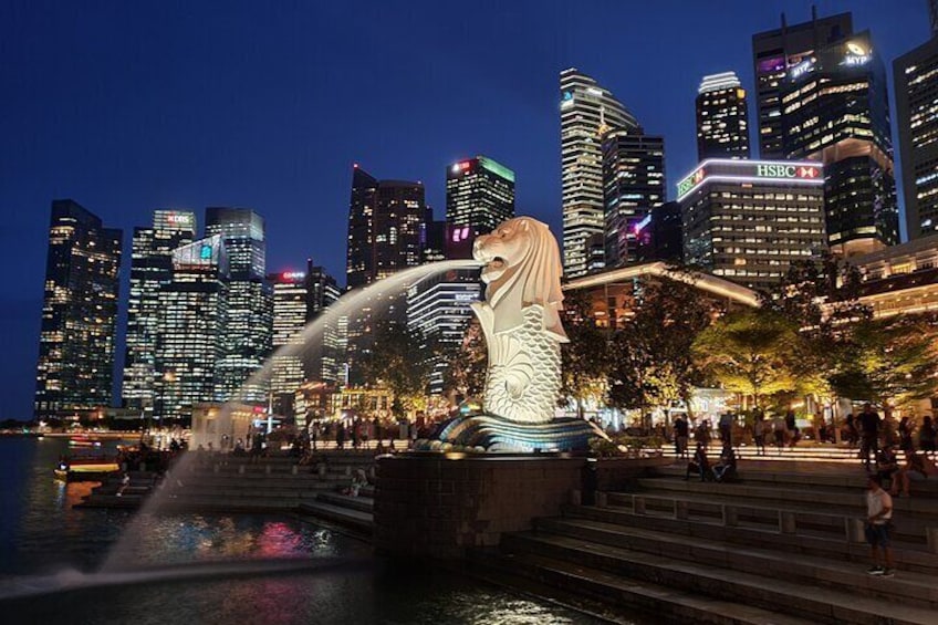 A cityscape with illuminated skyscrapers, a large dragon statue, and a fountain. 4