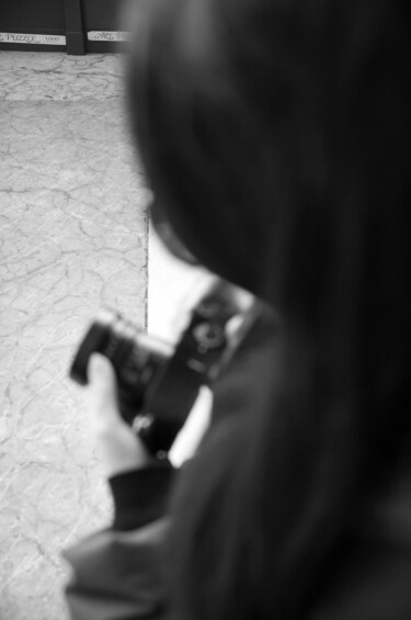 A person holding a camera, standing on a tiled floor with a blurred background. 2