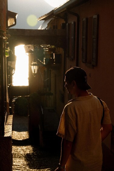 A person walking down a cobblestone street with buildings on either side and a bright light source in the background. 3