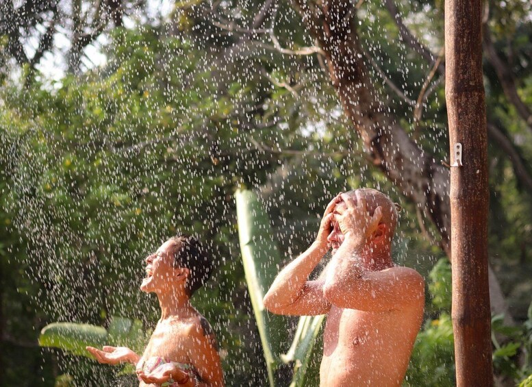 Two people enjoying a shower in a natural setting with trees and a wooden structure. 4