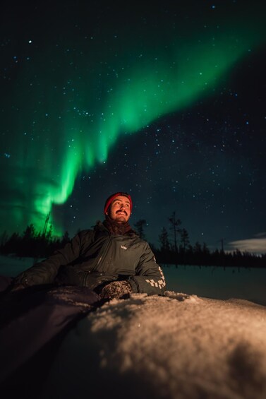 Une personne assise sur une surface enneigée, sous un ciel nocturne illuminé par des aurores boréales. 2