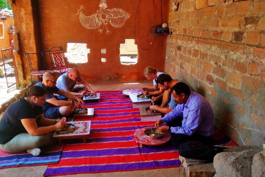 A group of people sitting on a colorful mat, eating from plates. 3