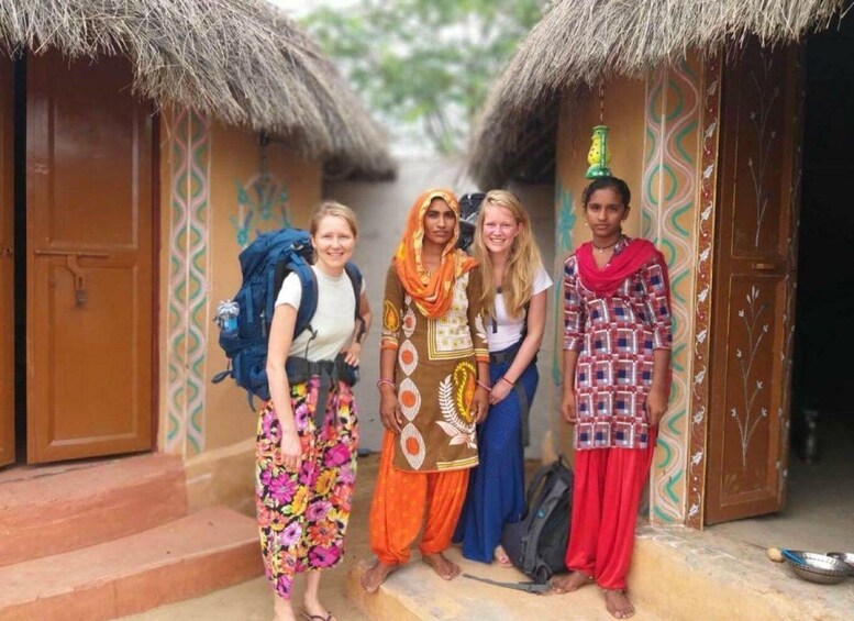 A group of people standing in front of traditional huts with thatched roofs and patterned walls. 1
