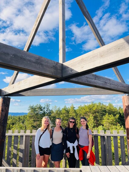 A group of people standing under a wooden structure with a forested landscape in the background. 5