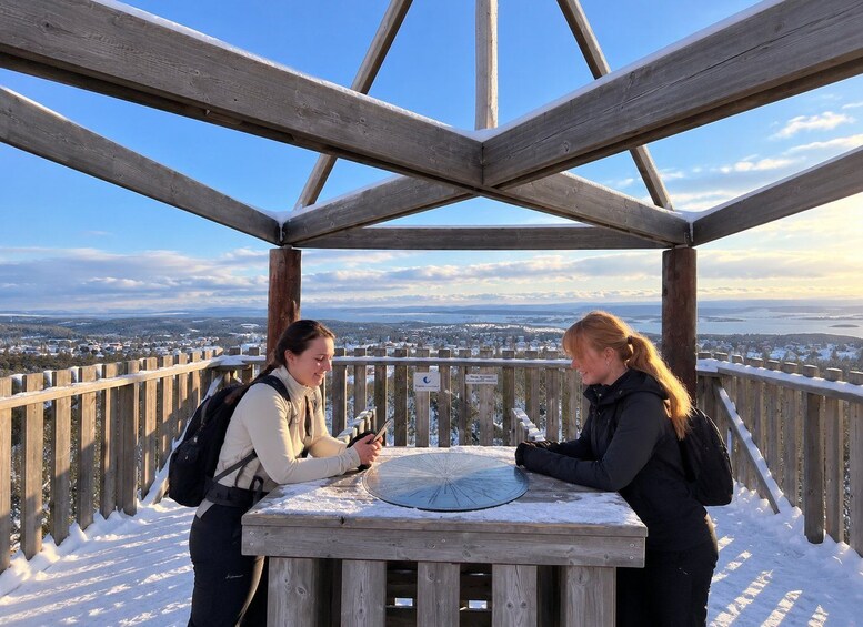 Two people at a wooden observation platform with a panoramic view of a snowy landscape. 4