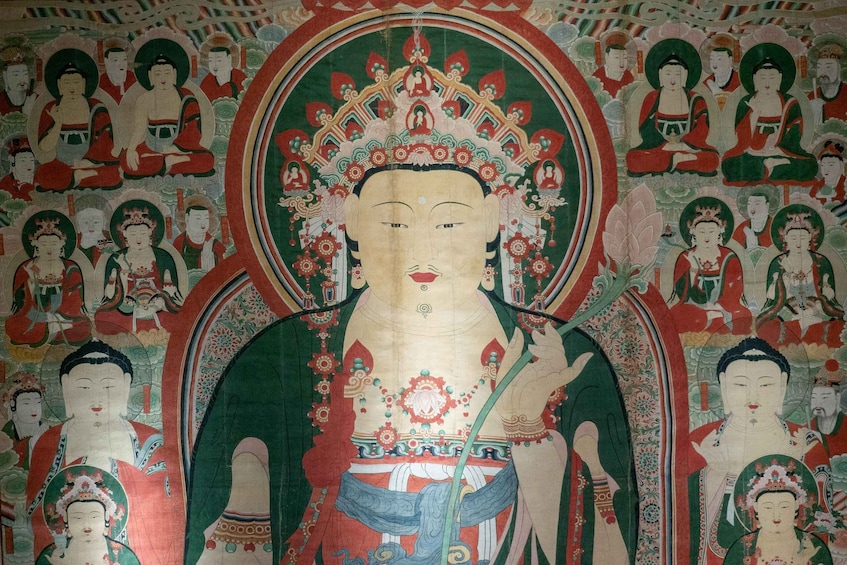 Une fresque murale représentant une figure centrale entourée de personnages plus petits, tous vêtus de costumes traditionnels. 2