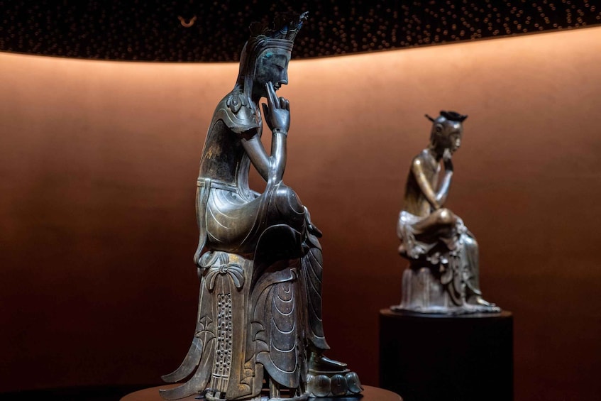 Deux statues en bronze représentant des personnages assis, exposées dans un musée. 1