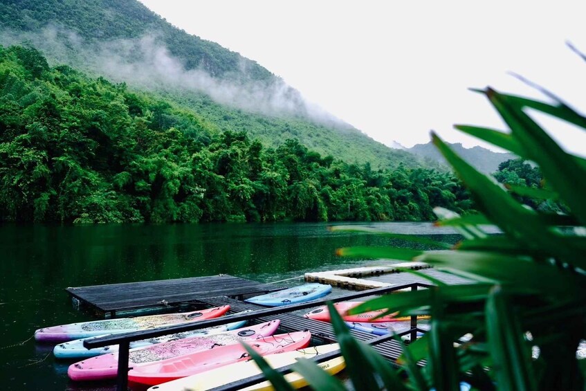 A calm river with kayaks docked on a wooden pier, surrounded by lush greenery and mist-covered hills. 4