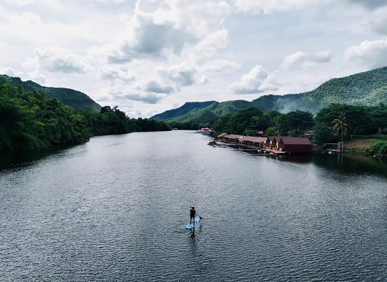 A person standing in a river with a surfboard, surrounded by lush greenery and hills. 2