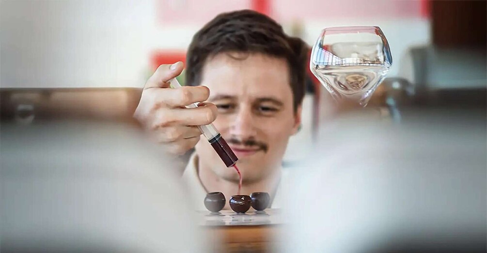 A person holding a wine glass with a red liquid, possibly wine, and a dropper. 2