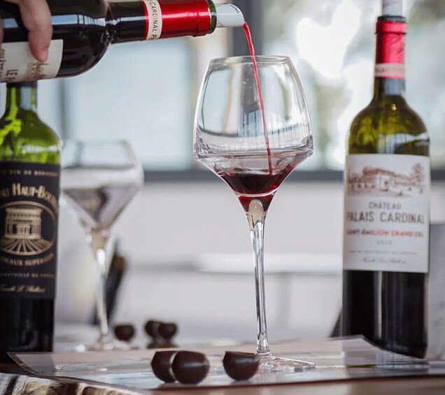 A bottle of Chateau Talais Cardinal wine being poured into a wine glass. 3