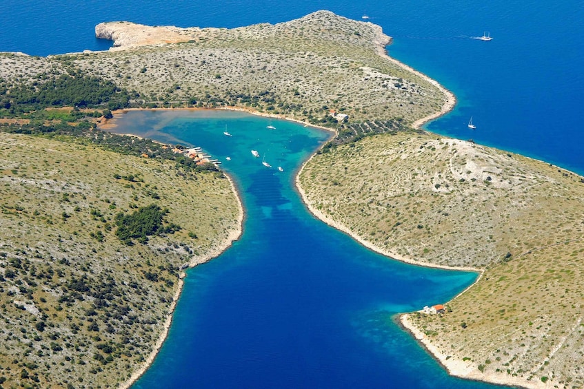 An aerial view of a coastal area with clear blue waters, a narrow inlet, and scattered boats. 1