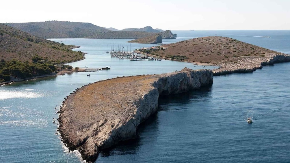 A coastal landscape with a large rock formation extending into the sea, a marina with boats, and distant hills. 3