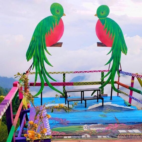 A colorful outdoor seating area with two large bird sculptures, a bench, and a patterned floor. 3